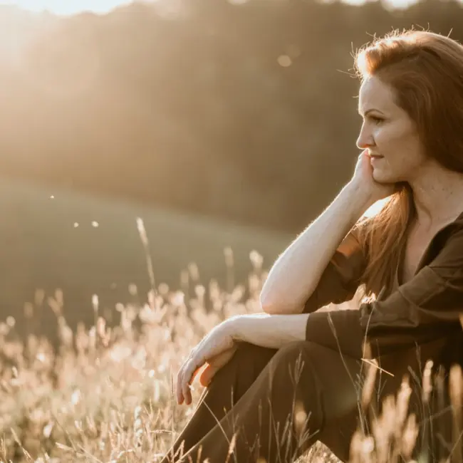Brigitte Adam sitzt nachdenklich in der Natur im goldenen Abendlicht - Adam Geschenke
