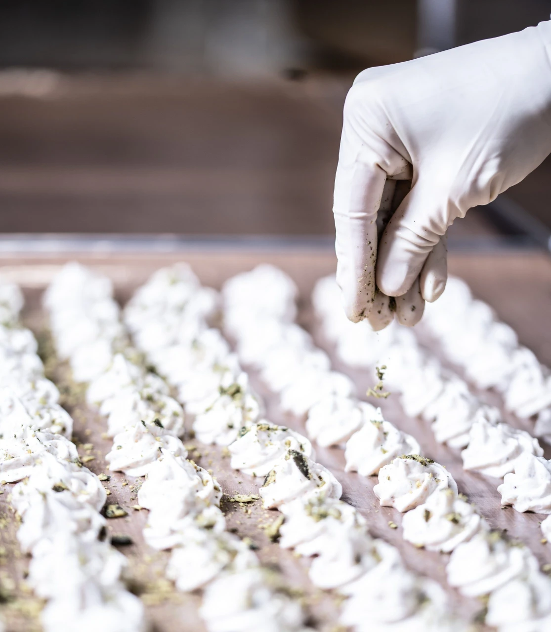 Hand bestreut frisch aufgespritztes Schaumgebäck mit Kürbiskernen in der Manufaktur Adam in der Südsteiermark