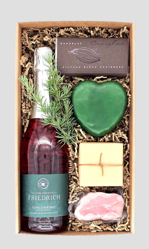 Herzhaftes Kundengeschenk aus Österreich in einer Geschenkbox mit Flasche, Schokolade, herzförmigem Produkt und dekorativen Naturmaterialien